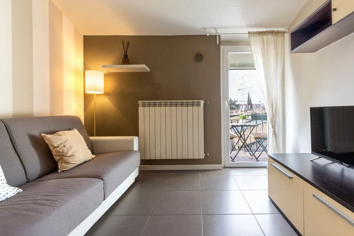 Una sala de estar con asientos, un televisor y una puerta de vidrio que da a un balcón.