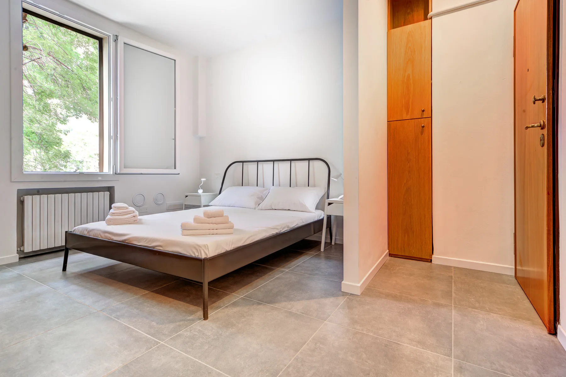Un dormitorio con una cama doble, toallas ordenadas y una ventana grande.