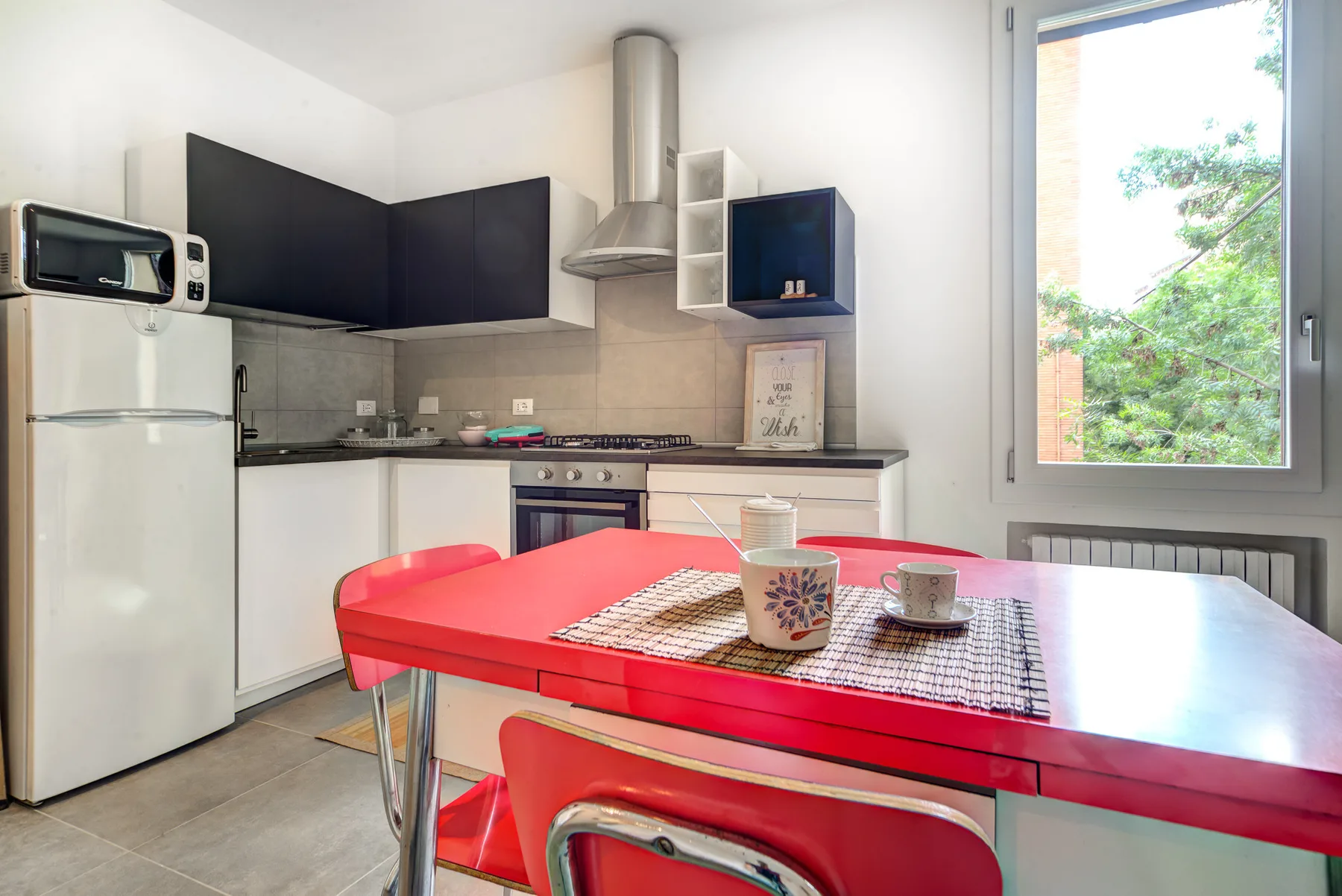 Una cocina y comedor luminosos, con una mesa roja junto a una ventana grande.
