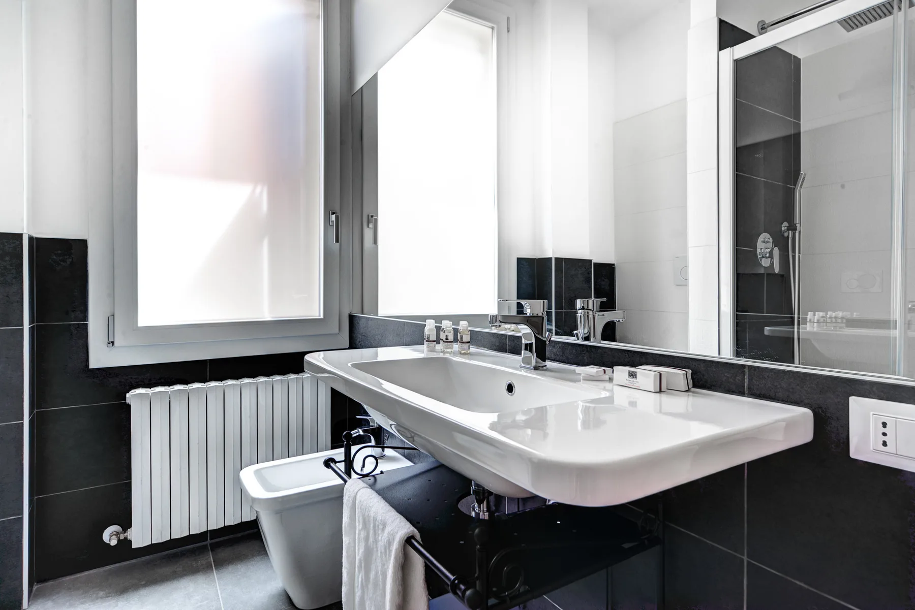 Un baño luminoso con un lavabo amplio bajo una ventana y una ducha cerca.