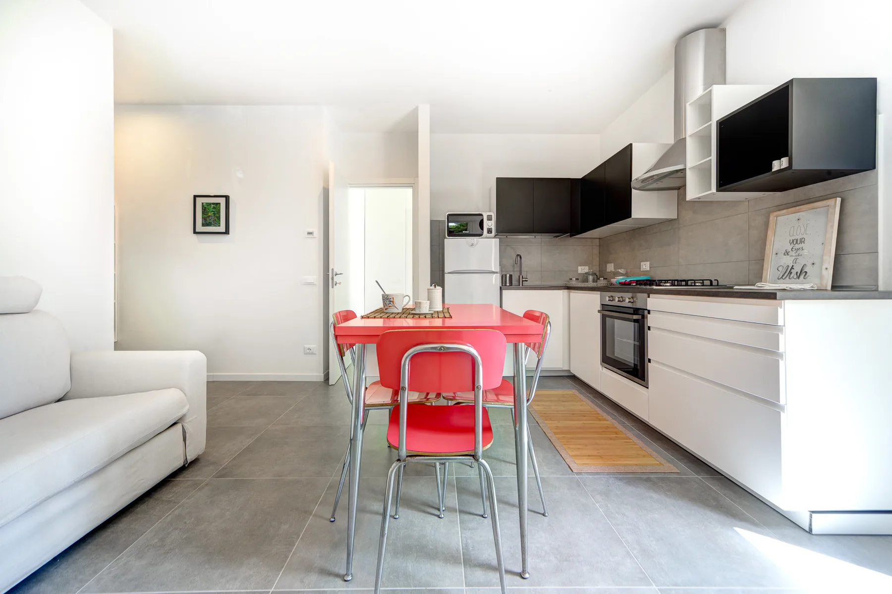 Una cocina luminosa con zona de comedor, mesa roja y asientos blancos.