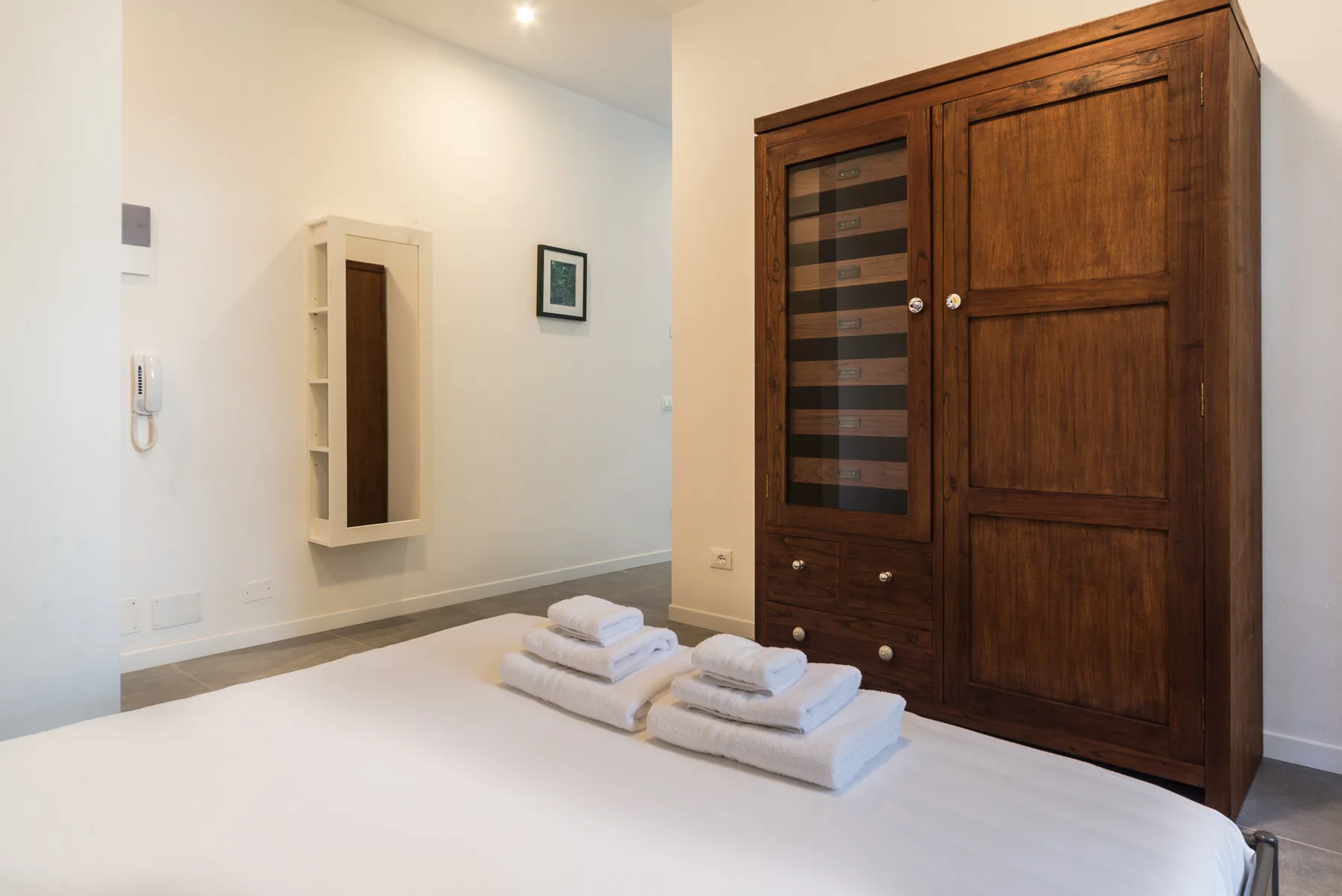 Un dormitorio con un armario grande de madera y toallas dobladas sobre la cama.