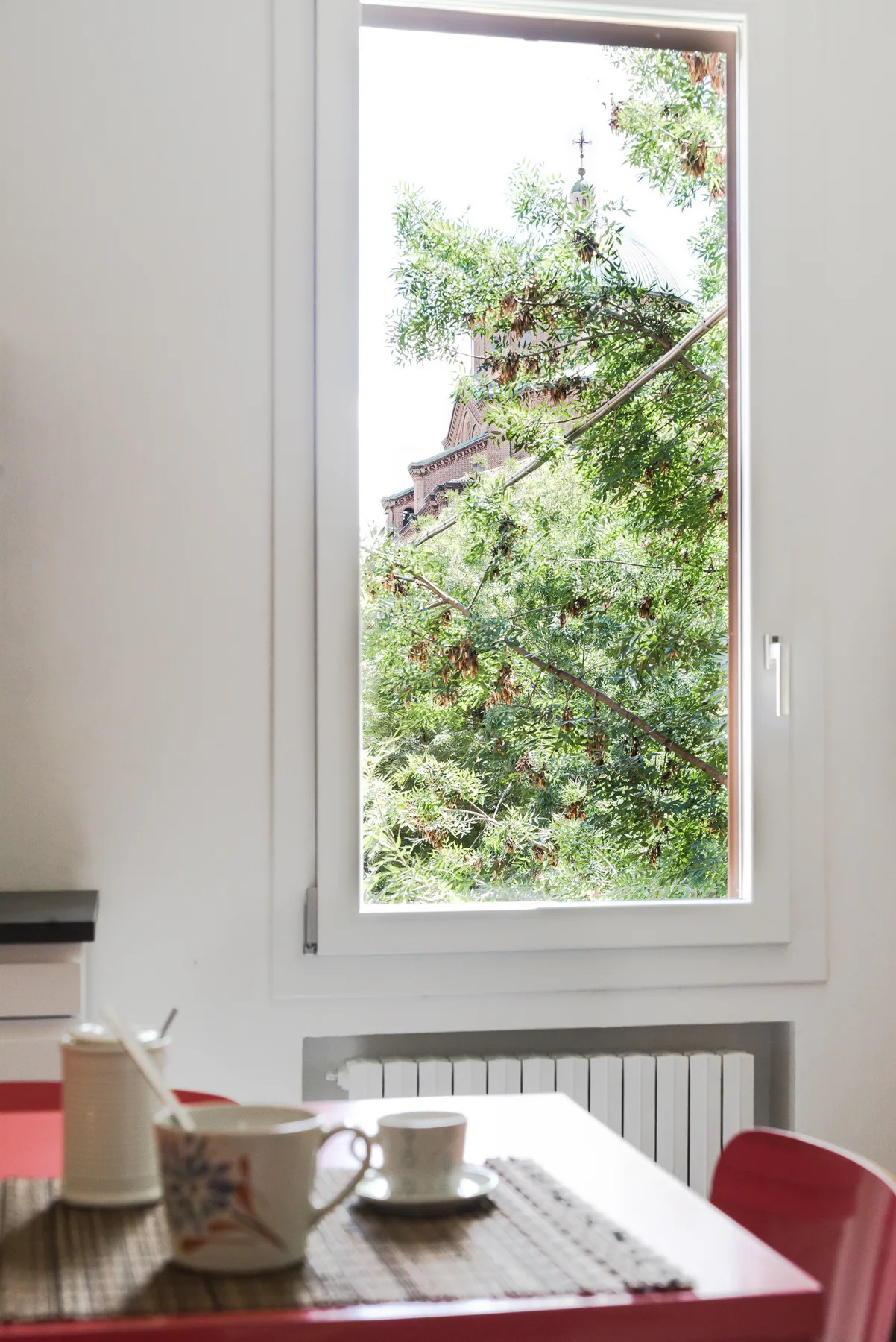 Un comedor con una mesa junto a una ventana grande con vista a árboles frondosos.