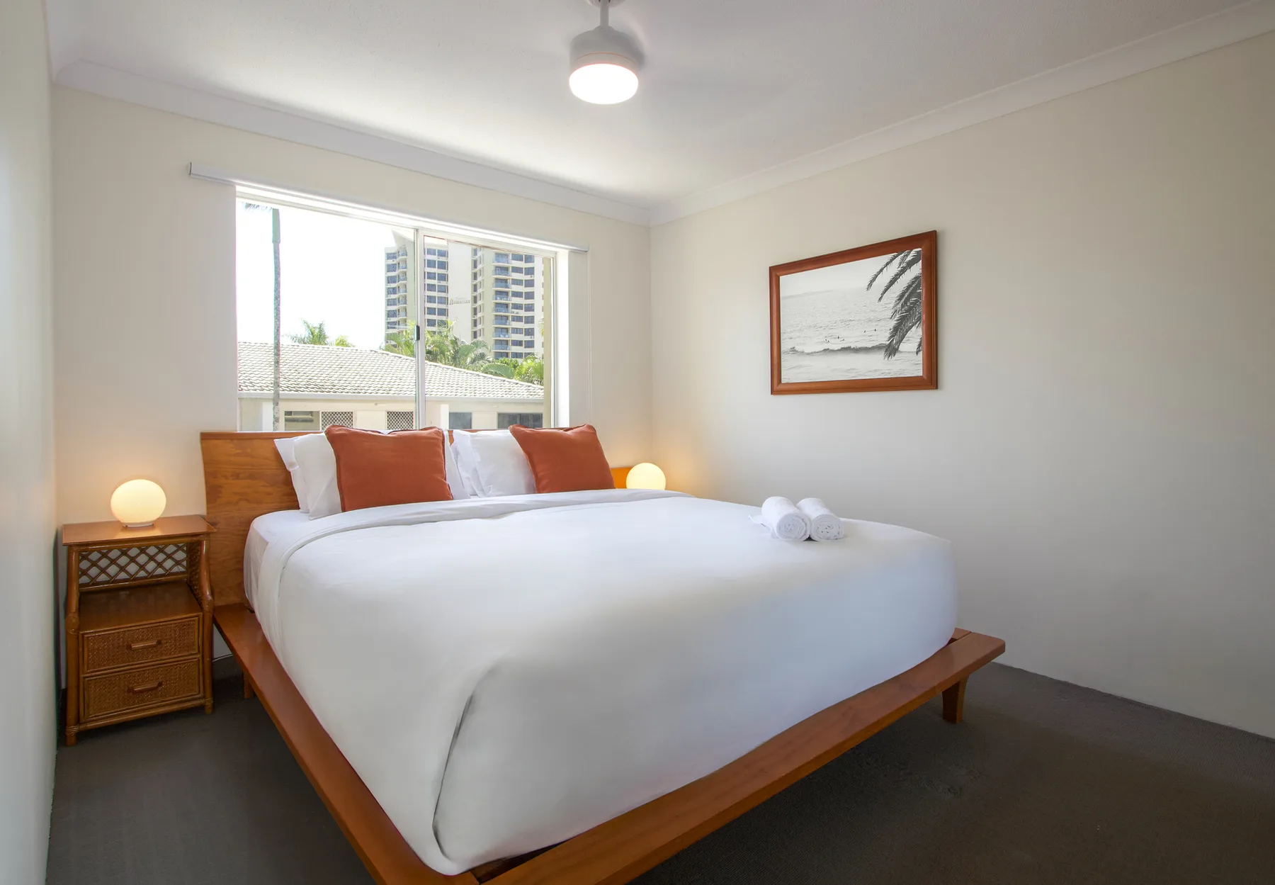 A bright bedroom with a neatly made bed beneath a large window.
