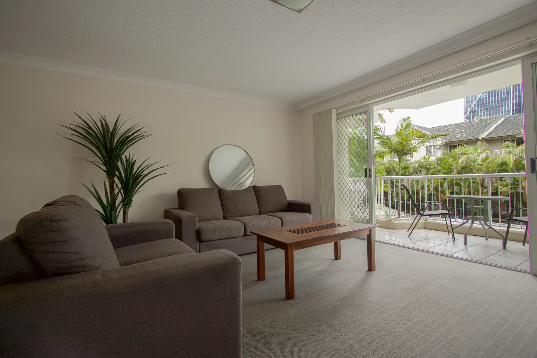 A living room opens onto a balcony with a view of greenery.