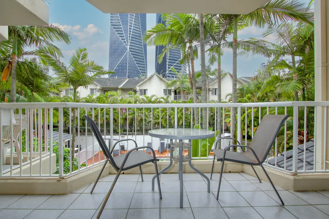 A balcony seating area overlooks palm trees and modern buildings.