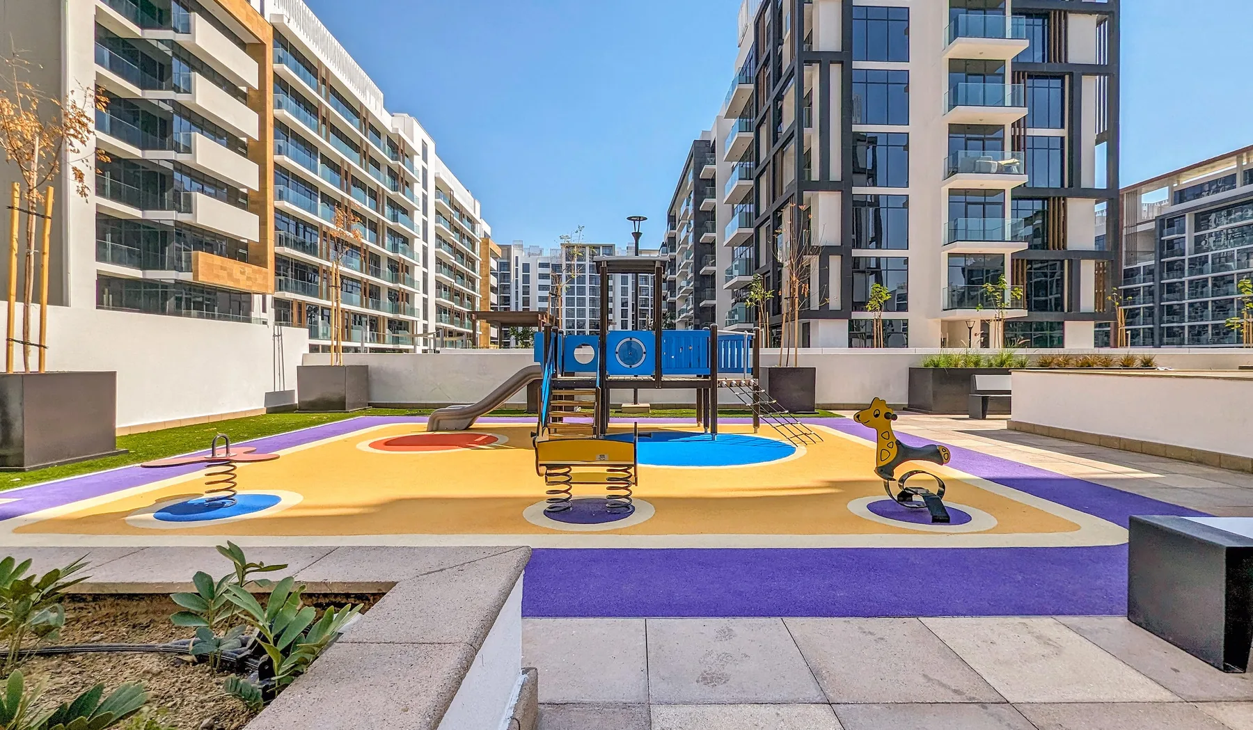 Un parque infantil colorido con juegos para trepar está entre edificios de apartamentos modernos.