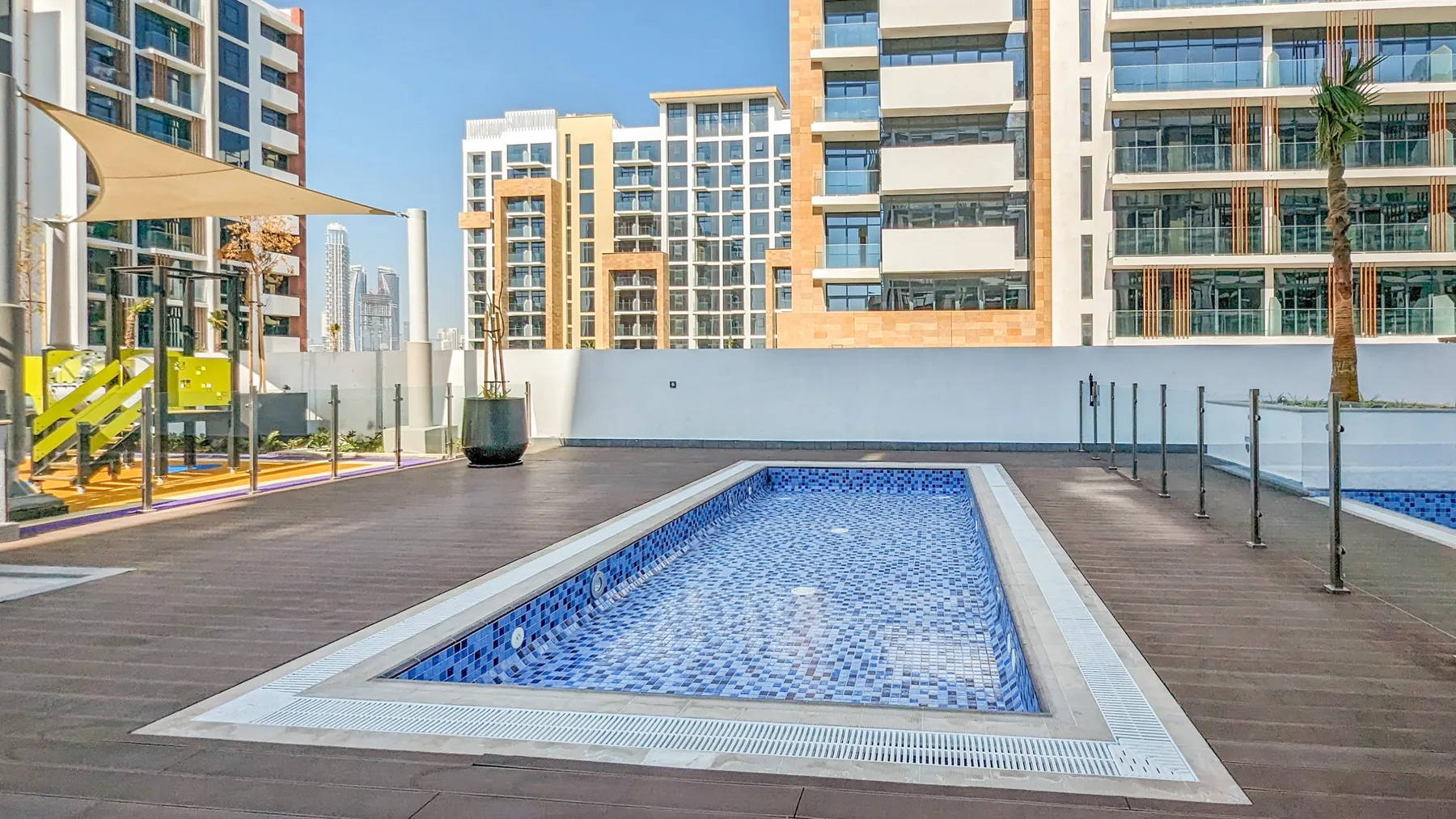 Una piscina exterior estrecha está en una terraza de madera entre edificios altos.