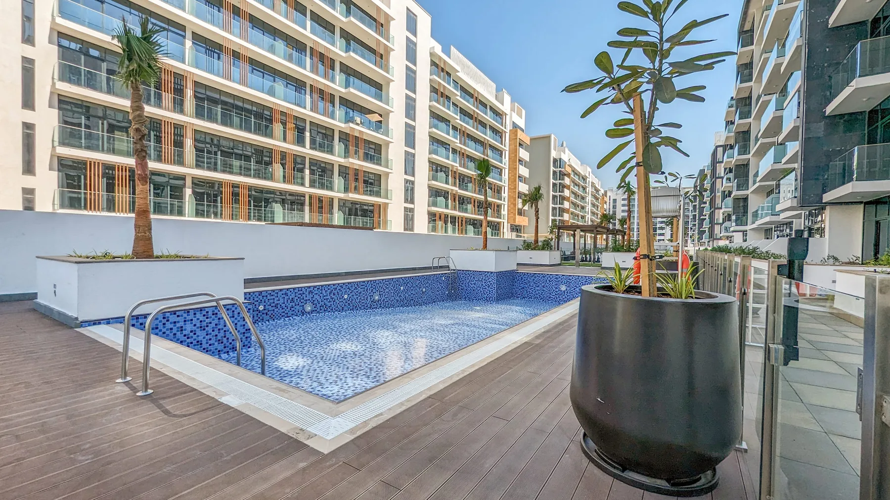 Una piscina al aire libre está rodeada de edificios de apartamentos modernos y jardineras.