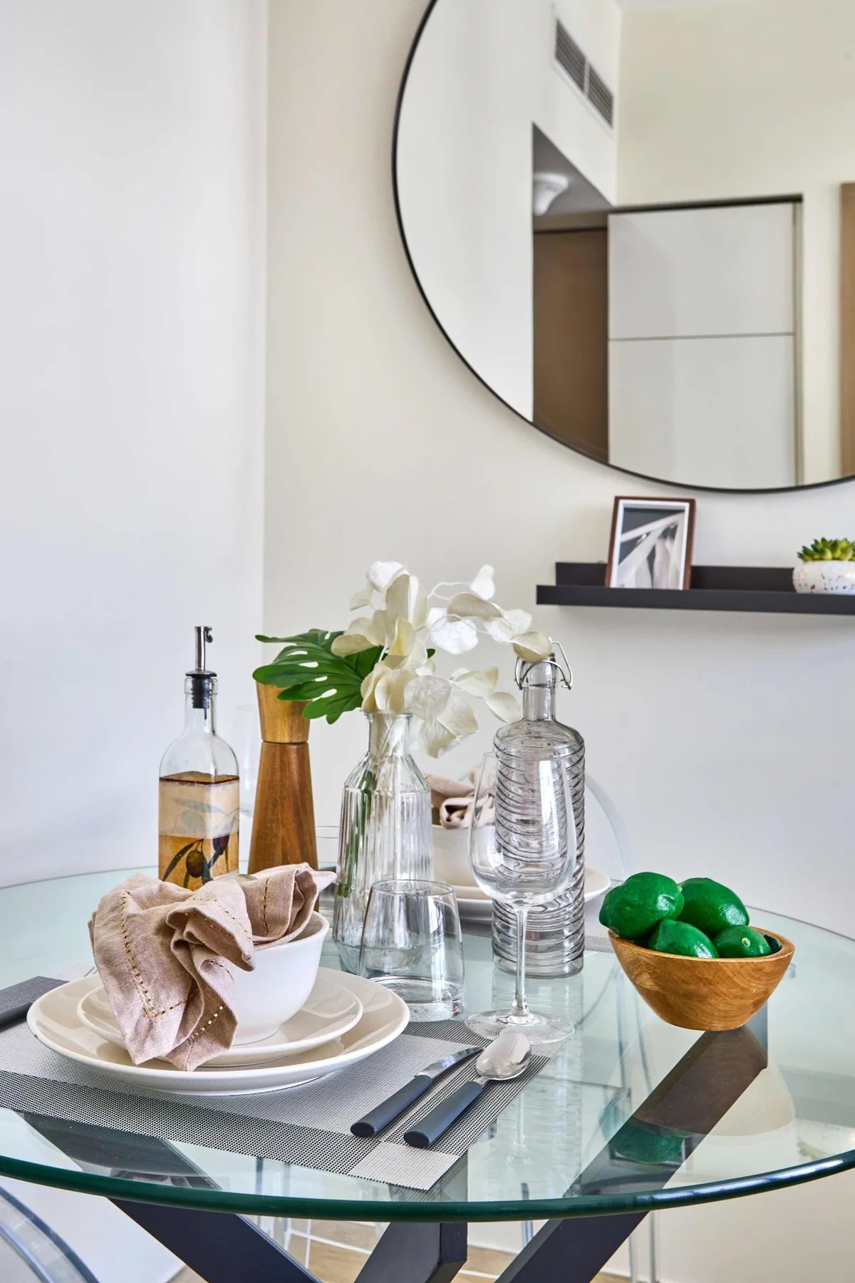 A dining table is set with plates, glassware, flowers, and a bowl of green fruit.