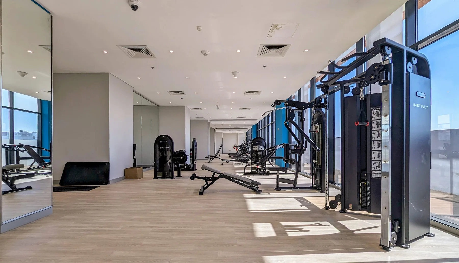 Un gimnasio con máquinas de ejercicio, estaciones de pesas y grandes ventanales.