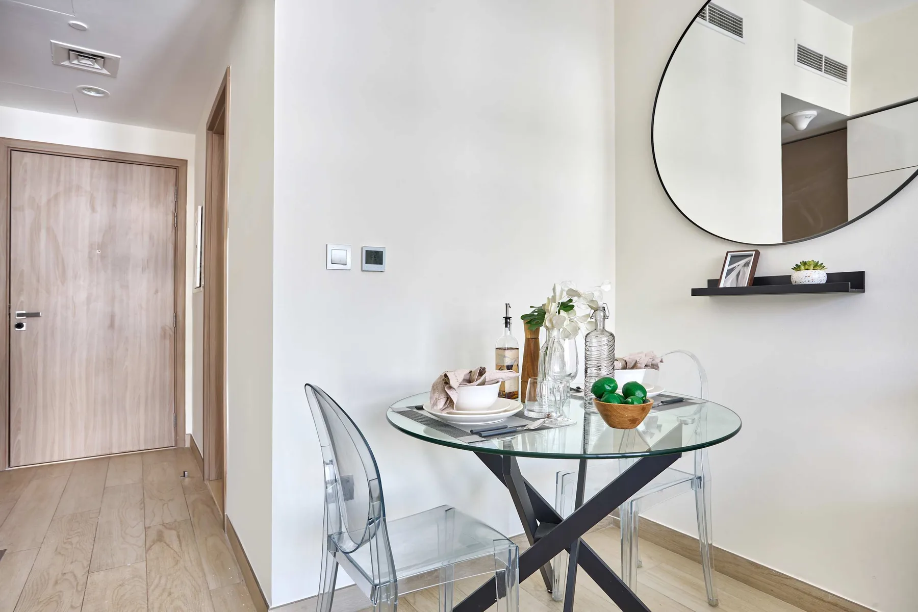 A dining area with a glass table and transparent seating beside a hallway.