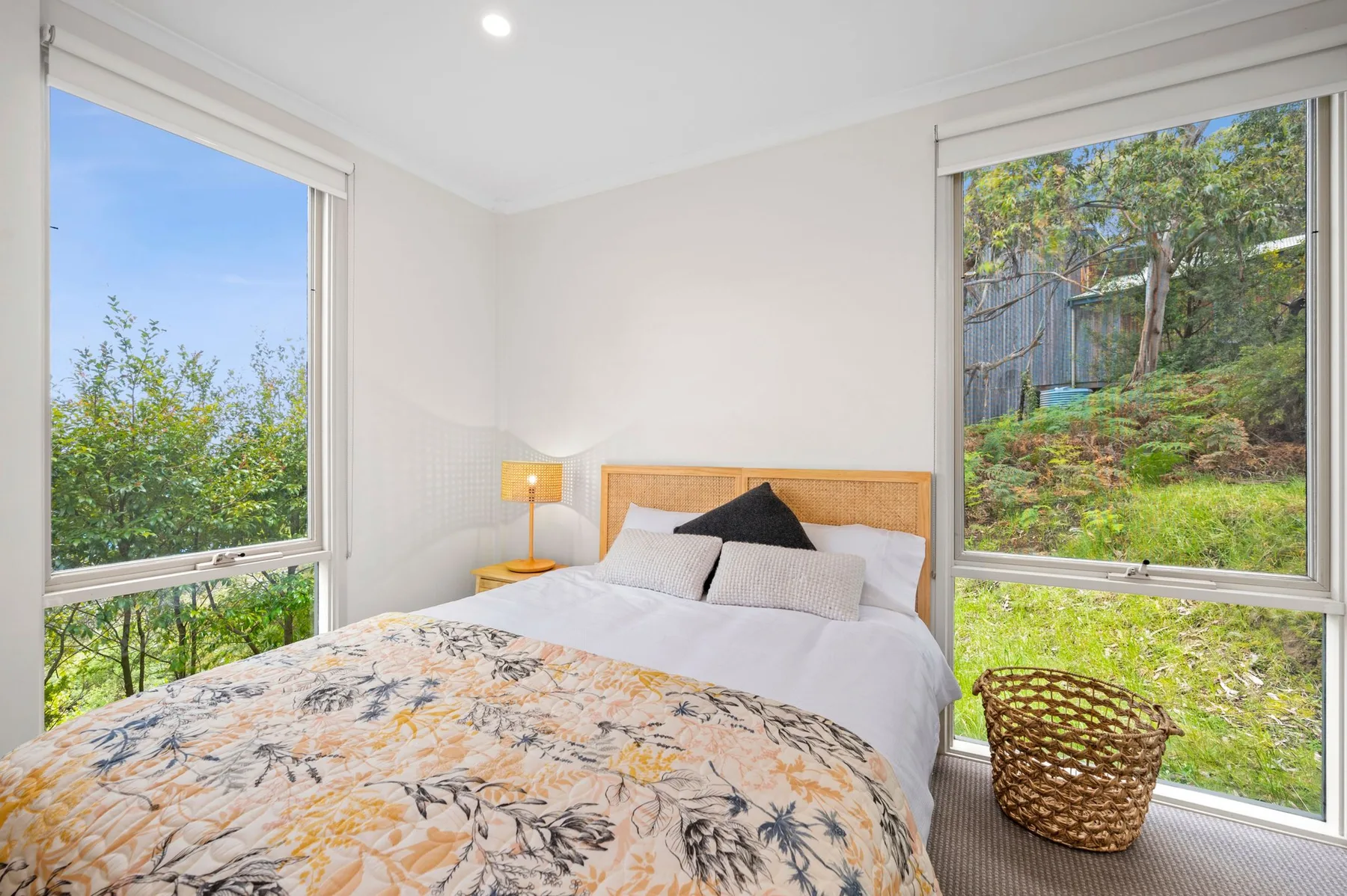 A bright bedroom with a bed and large windows overlooking greenery.
