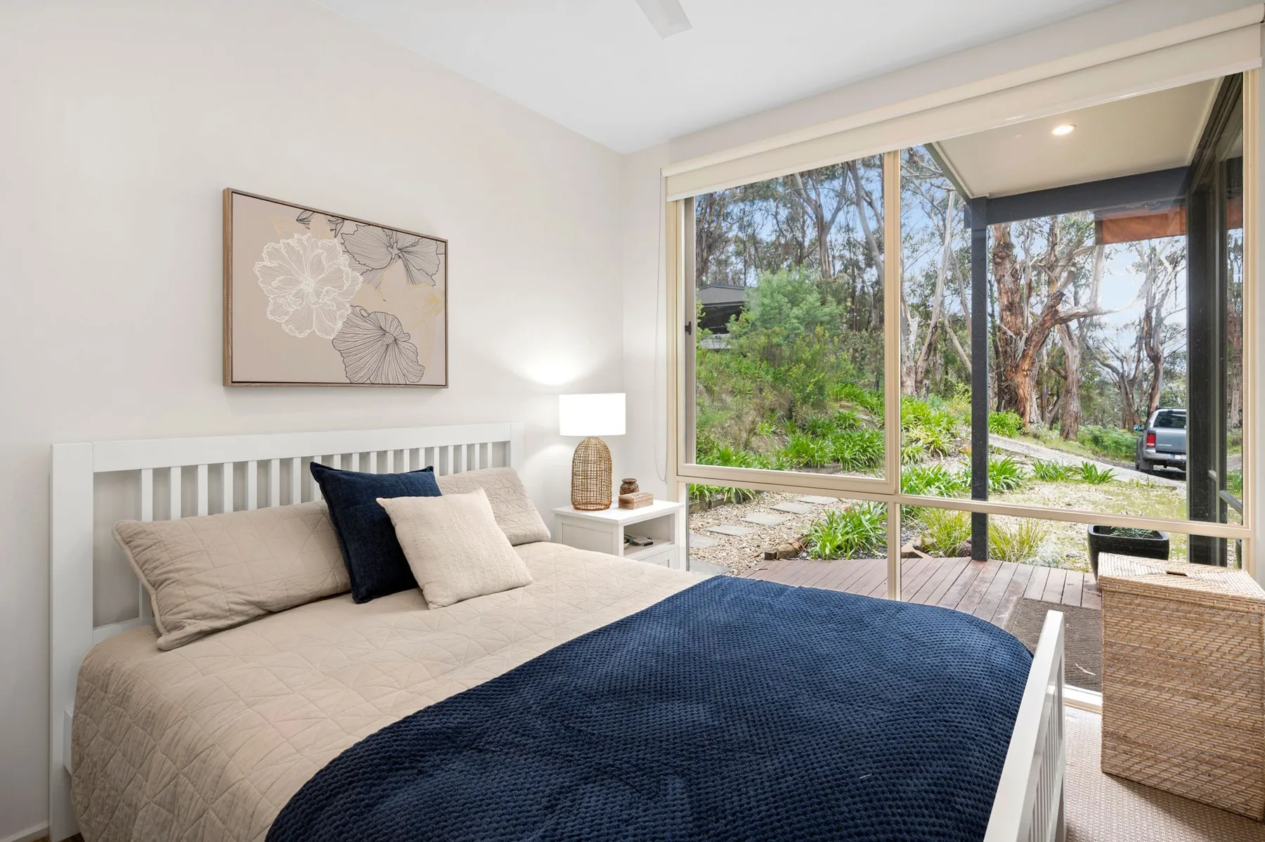 A bright bedroom with a bed facing large windows and greenery outside.