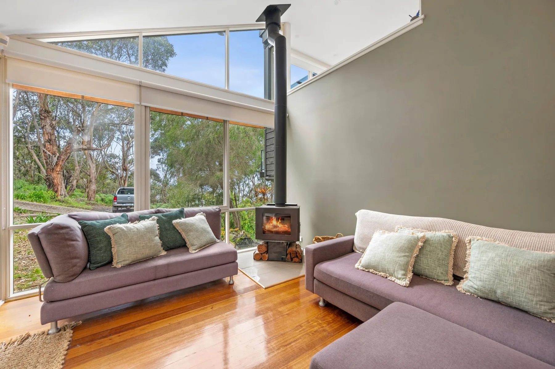 A bright living room with seating beside large windows and a wood-burning stove.