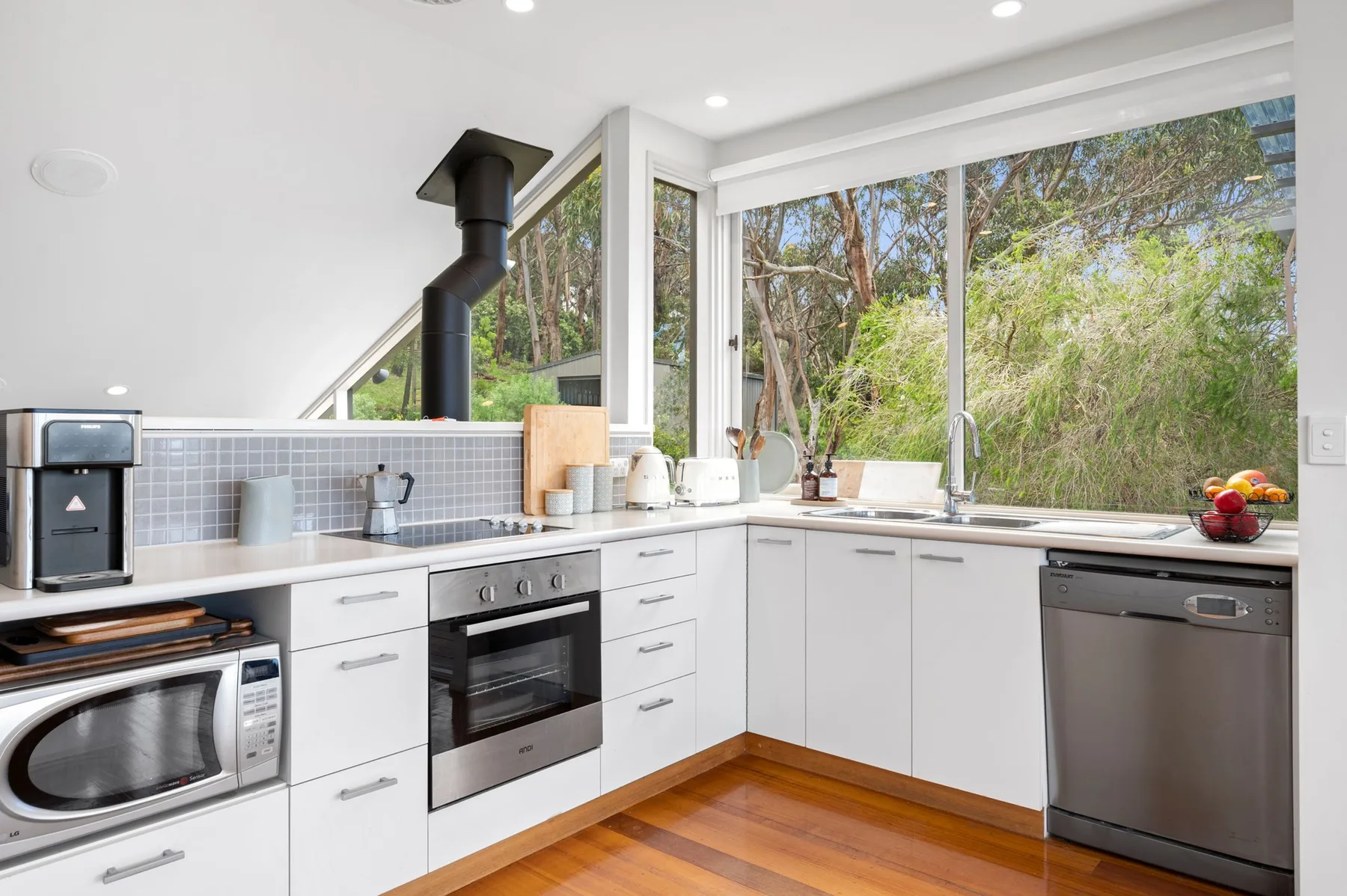 Una cocina moderna y luminosa con gabinetes blancos y grandes ventanas con vistas a la vegetación.