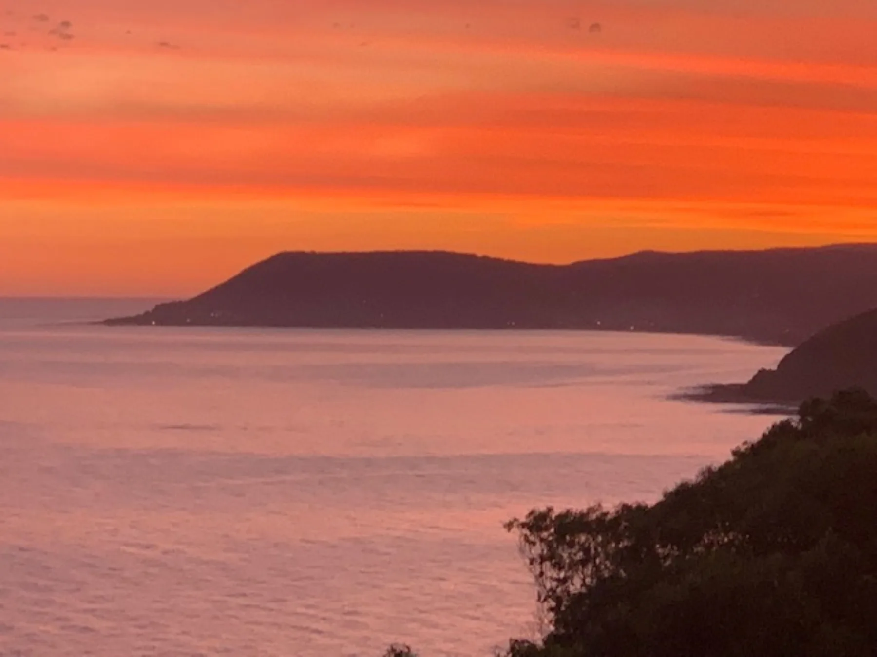 El atardecer ilumina el mar, con una costa oscura en el horizonte.