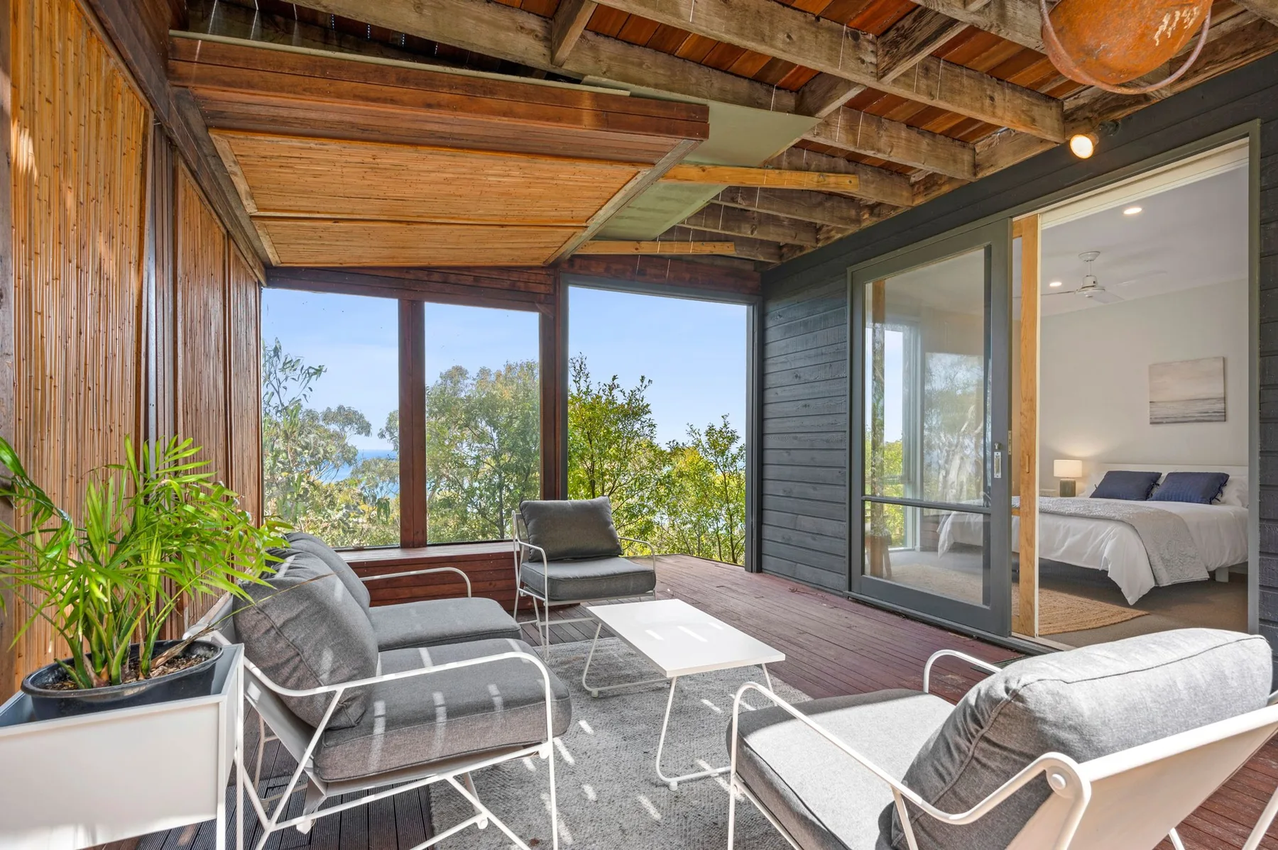 Una zona de estar exterior cubierta con grandes ventanas y vistas abiertas a los árboles.