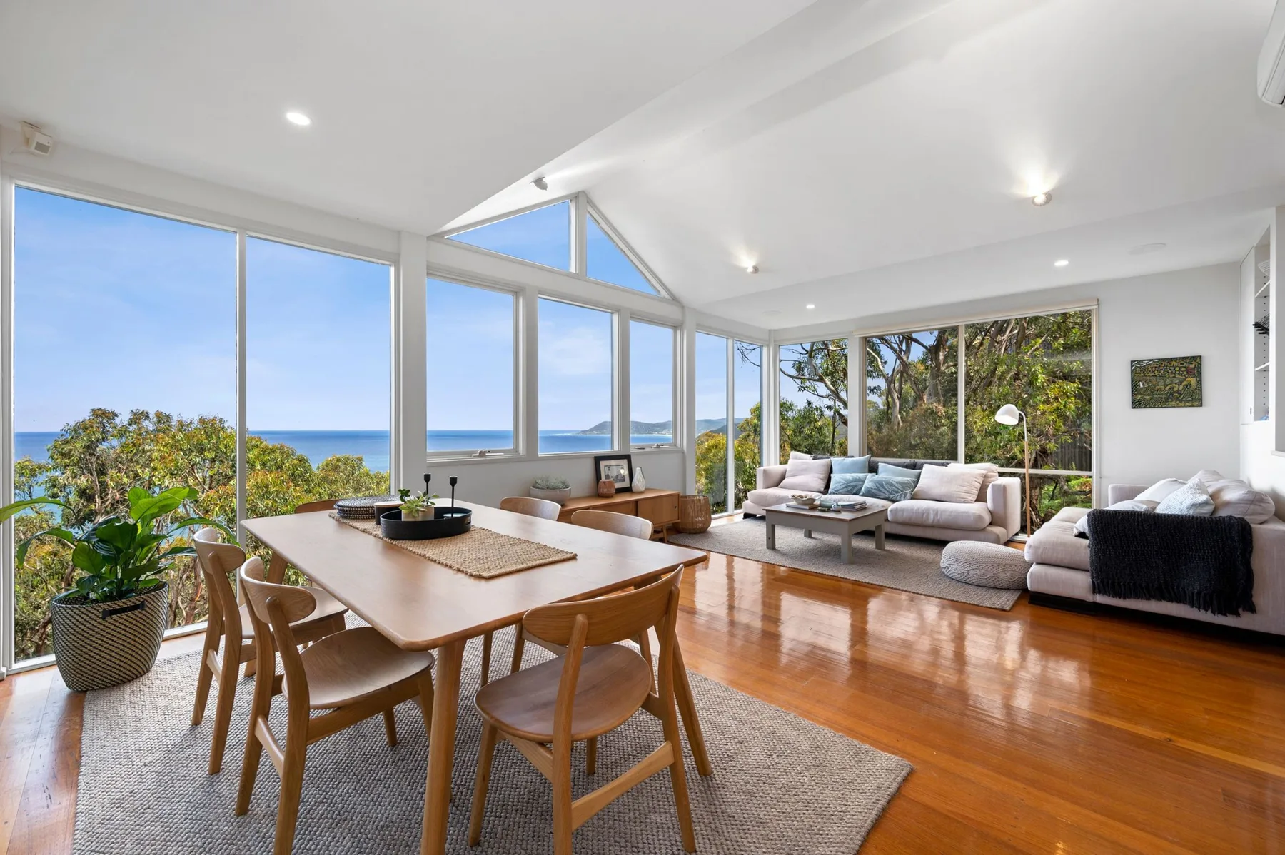 Una luminosa sala-comedor de concepto abierto tiene grandes ventanas con vistas al mar.
