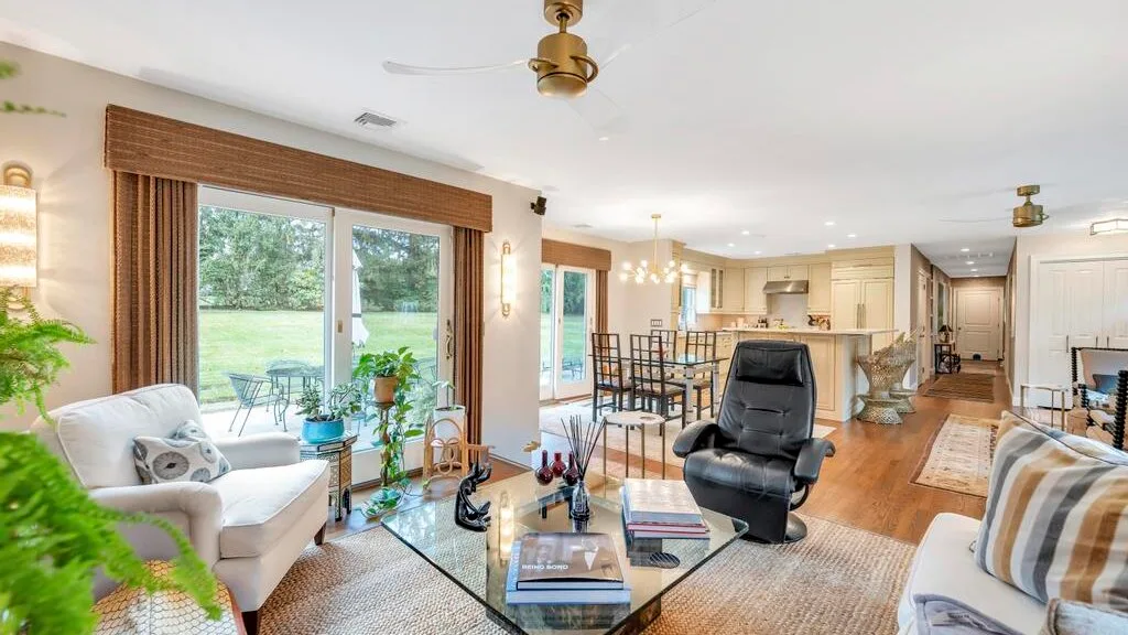 A bright open-plan living room with seating, a glass coffee table, and a dining area.