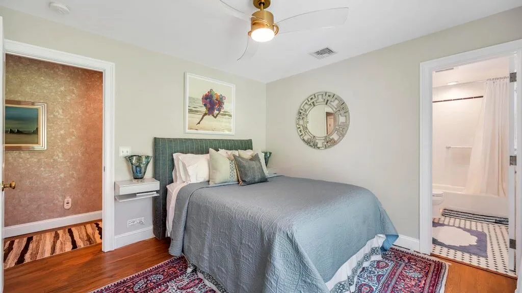 A bedroom with a bed, framed artwork, and an open doorway to a bathroom.