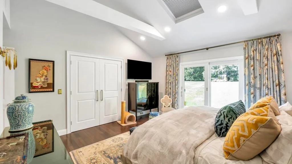 A bedroom with a large bed, patterned pillows, and curtains beside a bright window.