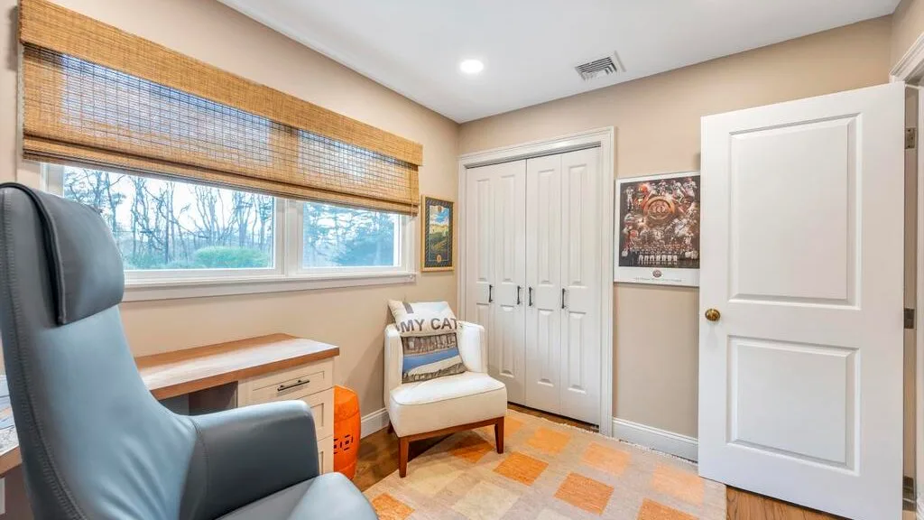 A bright room with a desk, a chair, and windows covered by woven blinds.