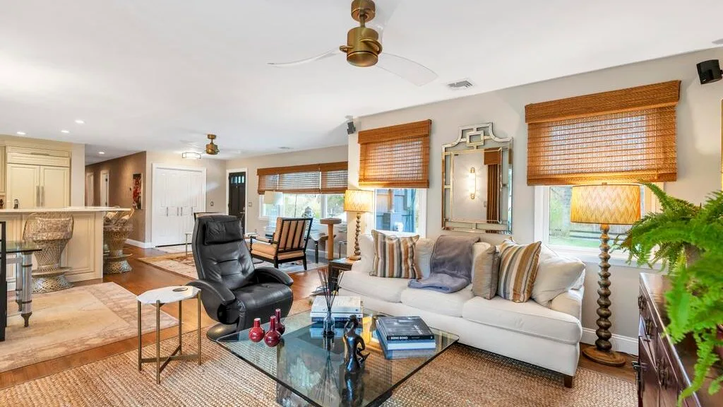 A bright living room with a white sofa, glass coffee table, and ceiling fan.