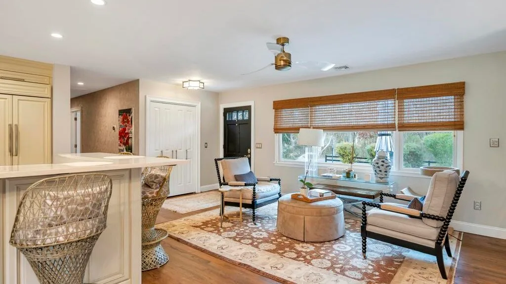 A bright living room with a seating area, large windows, and a patterned rug.