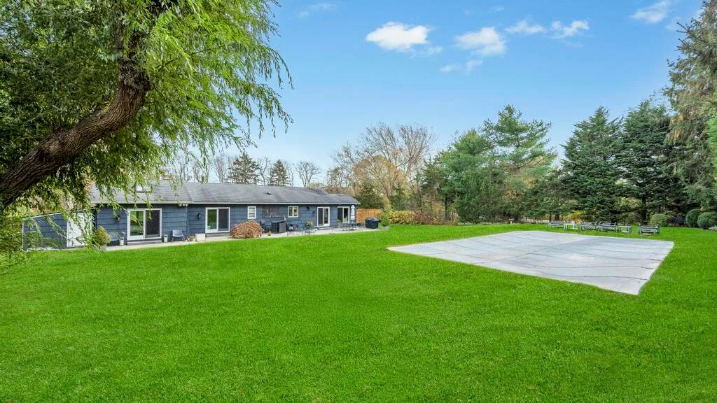 A single-story house sits beside a broad green lawn and paved patio.