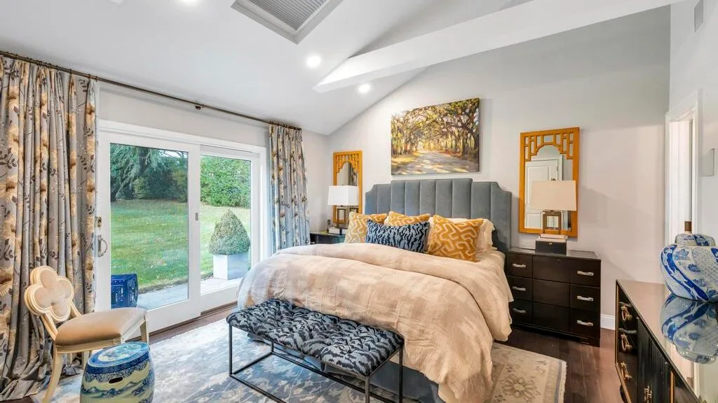 A bedroom with a bed, patterned curtains, and glass doors opening onto a garden.
