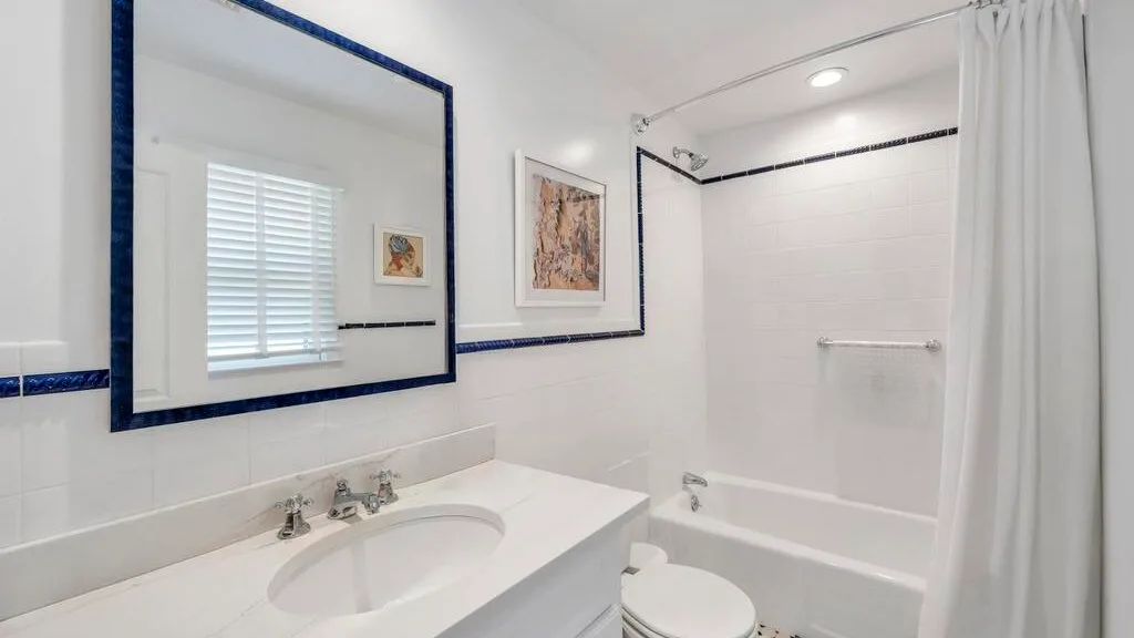 A bright bathroom with a sink, mirror, and bathtub behind a shower curtain.