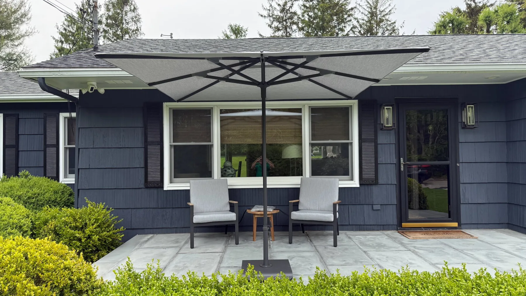 A patio seating area sits outside a dark-sided house beneath a large umbrella.
