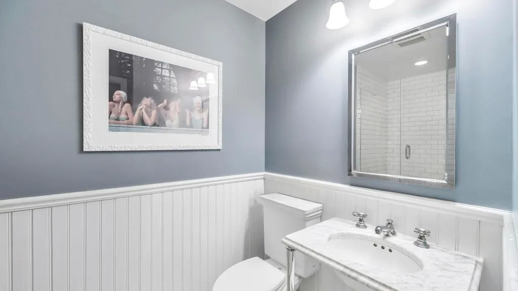 A bathroom vanity with a sink and mirror above white paneled wainscoting.