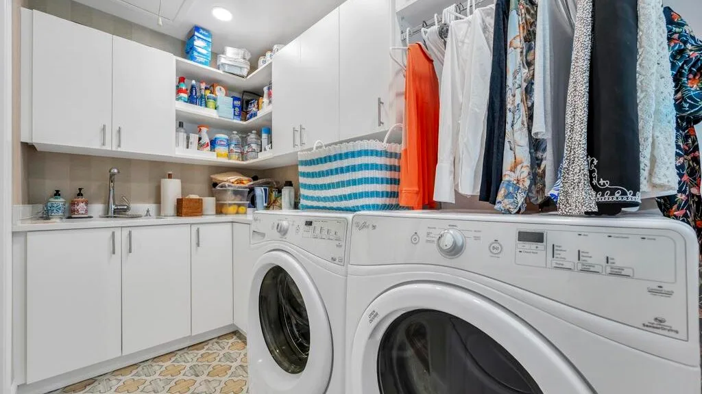 A laundry room with washing machines, cabinets, and hanging clothes.