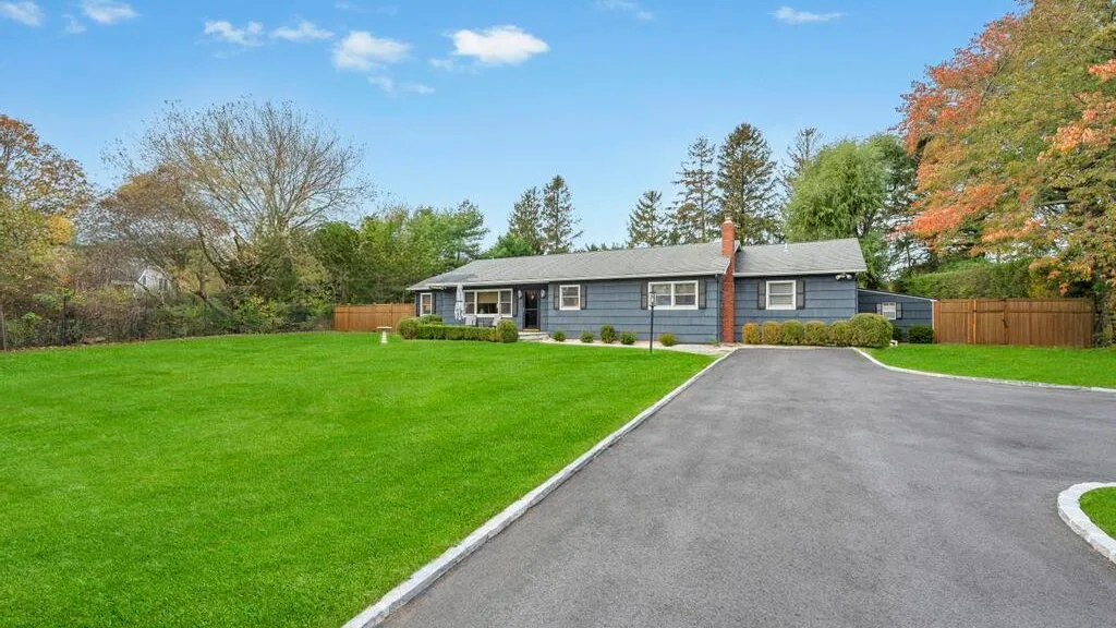 A single-story house stands beside a paved driveway and broad green lawn.
