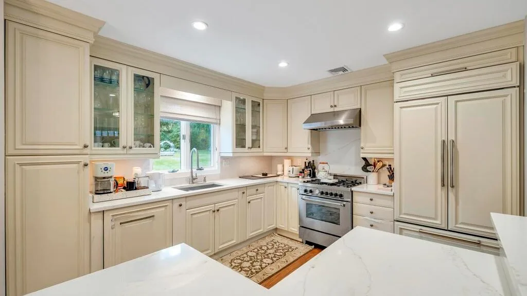 A bright kitchen with cream cabinetry, a cooking range, and marble-look counters.