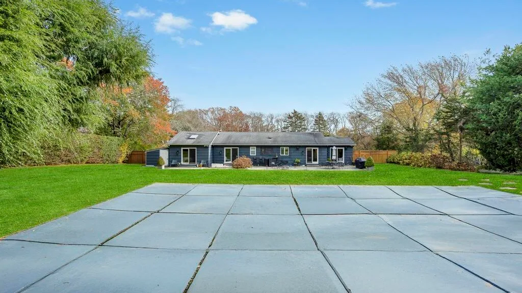 A paved patio overlooks a lawn and a single-story house.