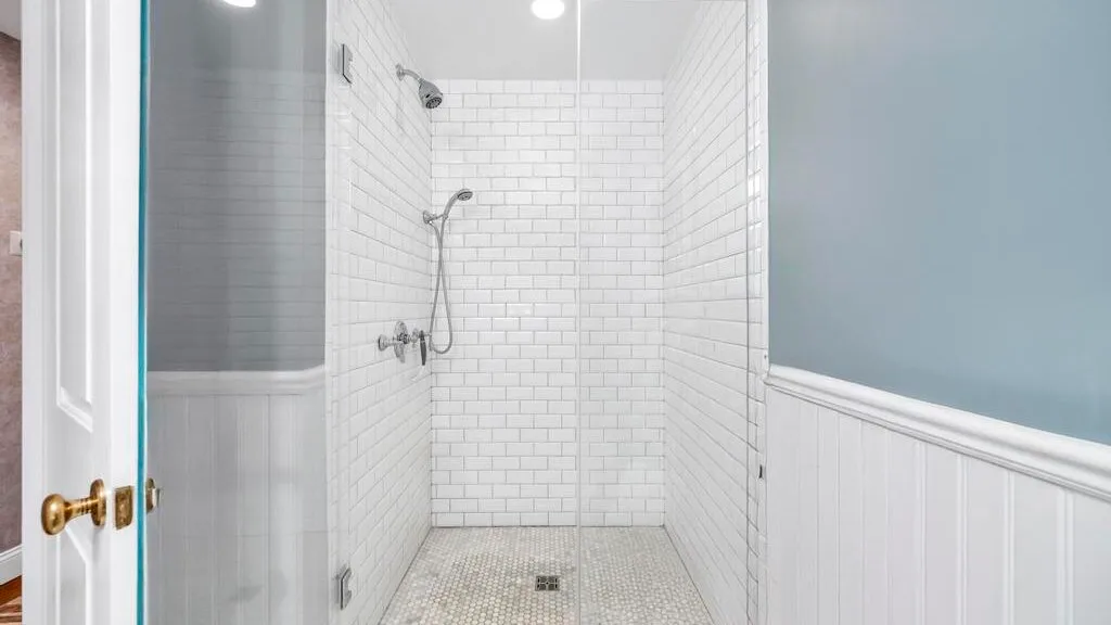 A tiled bathroom shower with white walls and a small floor drain.