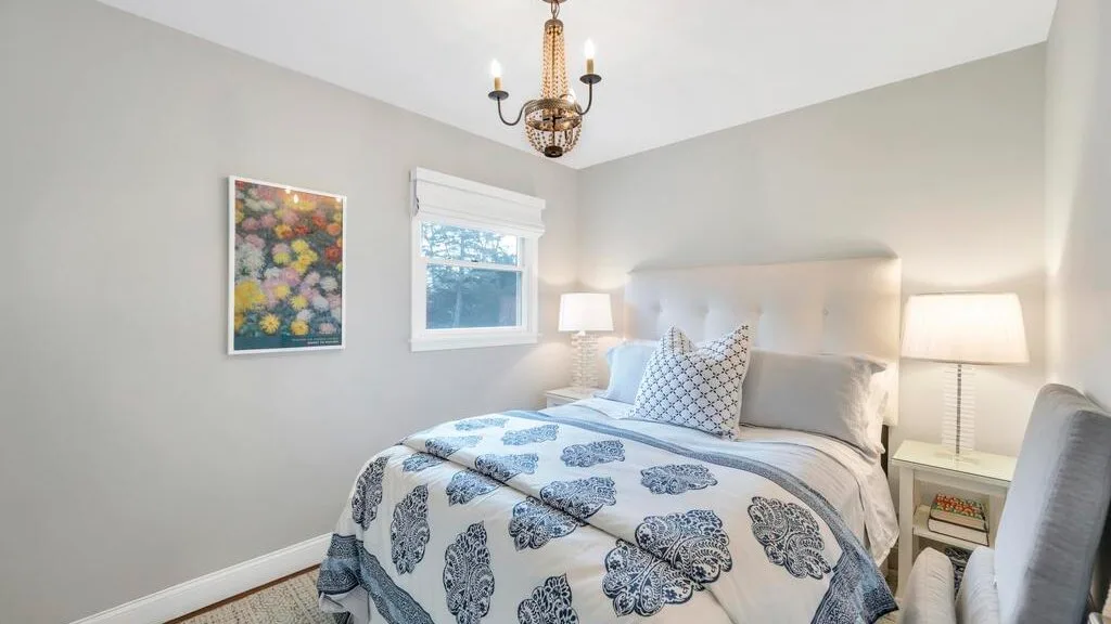 A bright bedroom with a patterned bedspread and framed floral artwork.