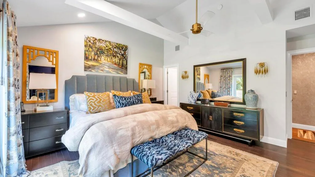 A bedroom with a large bed, dark dressers, and a patterned rug.