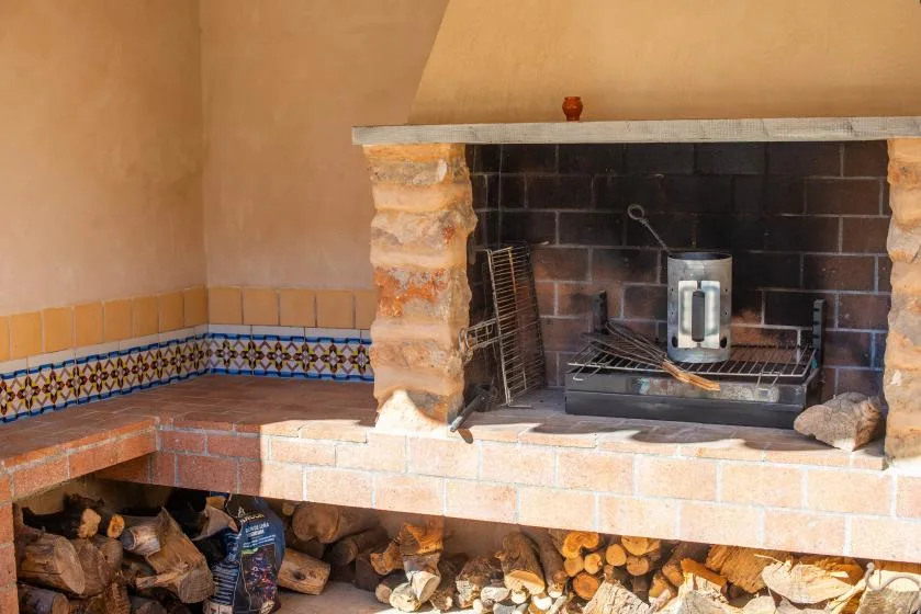 A rustic fireplace with a tiled hearth and stacked firewood below.