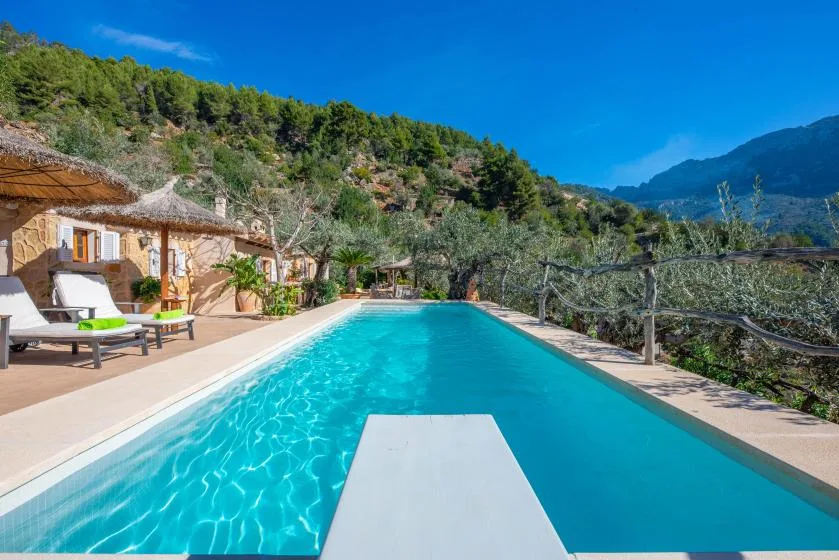 An outdoor swimming pool beside a hillside house, with loungers along the edge.