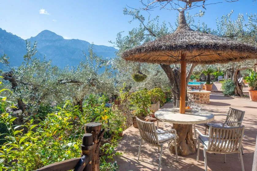 An outdoor patio with a shaded table and mountain views beyond the garden.