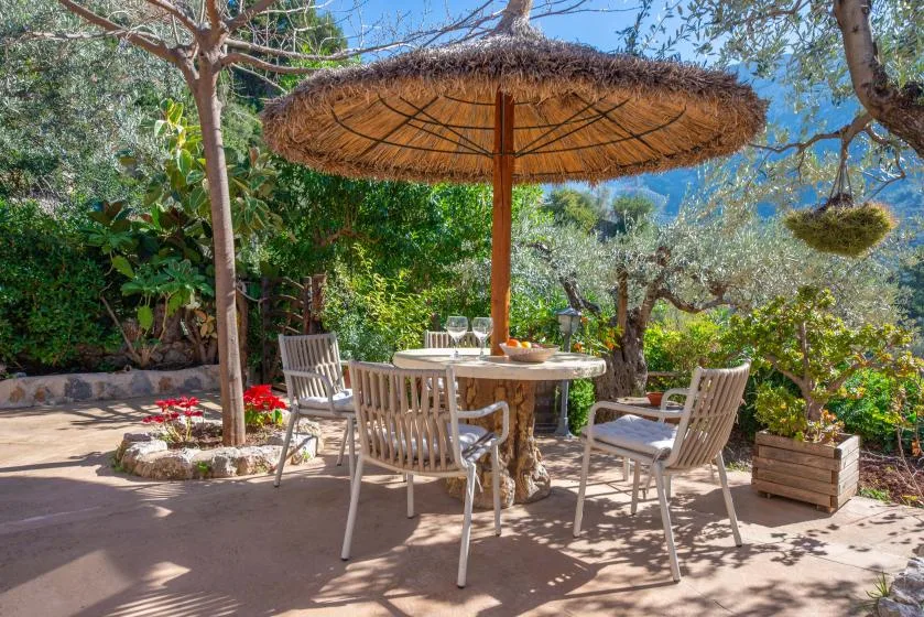 An outdoor dining area with a round table beneath a large thatched parasol.