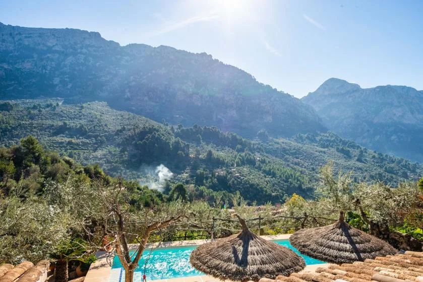 A swimming pool sits below a green mountain landscape.