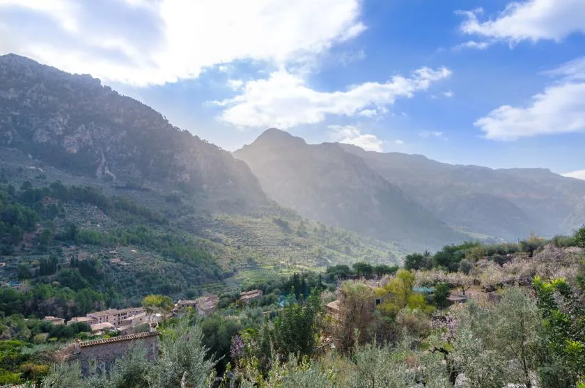 A mountain valley with green slopes beneath a partly cloudy sky.