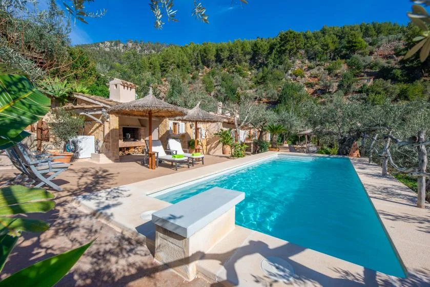 An outdoor swimming pool beside a patio, with wooded hills in the background.