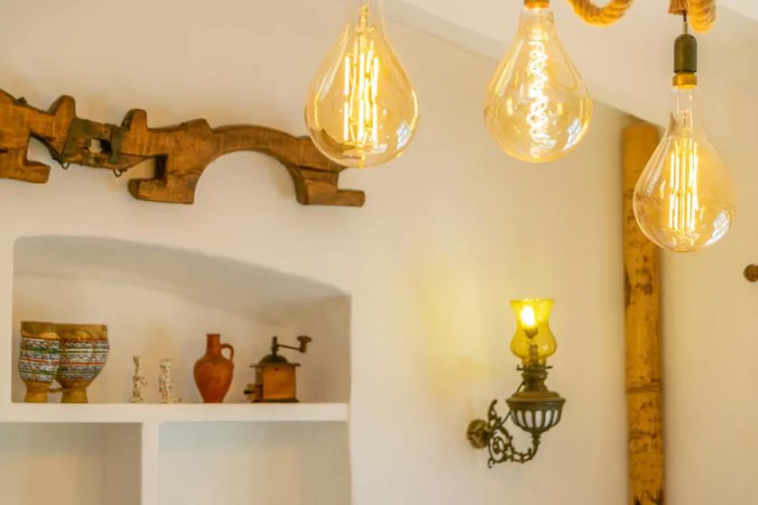 A warmly lit interior wall has decorative shelves, pottery, and hanging pendant lights.