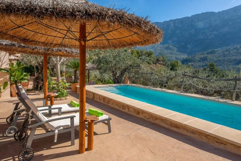 An outdoor pool beside a shaded patio with loungers and mountain views.
